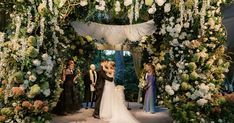 the bride and groom are kissing under an arch covered with white flowers at their wedding ceremony