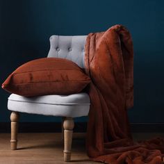 a white chair with a brown pillow on it and a blanket draped over the back