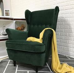 a green chair with a yellow blanket on it in front of a white brick wall