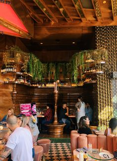 people sitting at tables in a restaurant with lots of greenery hanging from the ceiling