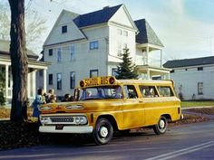 an old yellow school bus parked in front of a house with people standing around it