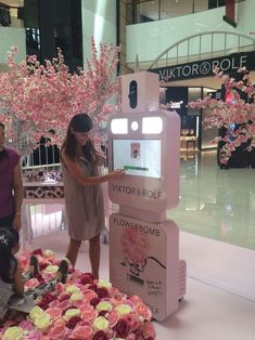 two people standing in front of a display with pink flowers on it and a sign that says victoria & rolle flowerboom