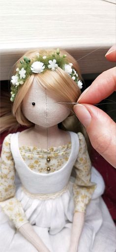 a hand holding a doll with flowers in it's hair