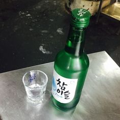 a green bottle sitting on top of a metal table next to a glass cup and container