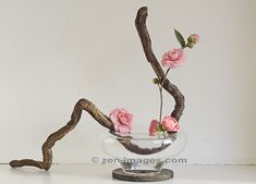 a glass bowl filled with pink flowers on top of a white table next to a branch