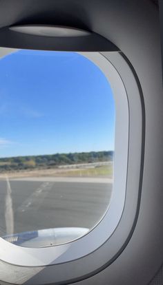 the view from inside an airplane window looking out at the runway and trees in the distance