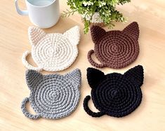 four crocheted cat coasters sitting next to a coffee cup