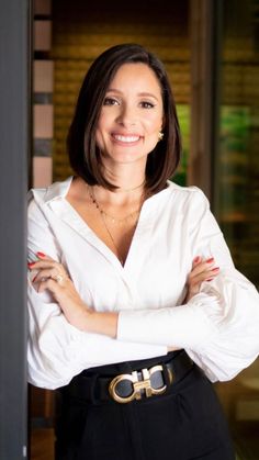 a woman in white shirt and black pants with her arms crossed posing for the camera