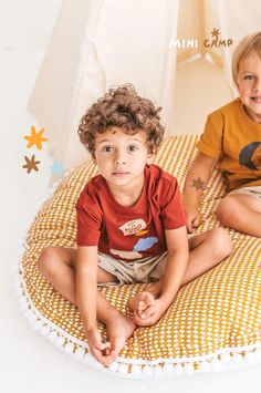 two young boys sitting on the floor in front of a tent