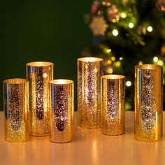 gold candles are lined up on a table near a christmas tree and lite - up lights