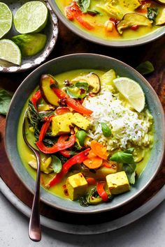 two bowls filled with vegetables and rice on top of a wooden table next to limes