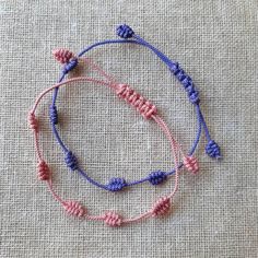 two bracelets with pink and blue beads are sitting on a piece of linen fabric