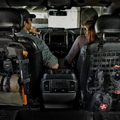 two people sitting in the back of a vehicle with their gear on and one person standing next to them