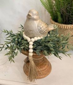 a bird statue sitting on top of a vase filled with green leaves and beads next to a potted plant