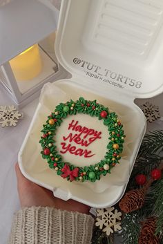 a person holding up a cake in a box with the words happy new year written on it