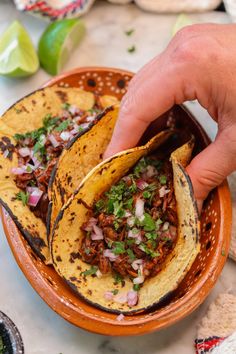 a hand is picking up some tacos from a bowl