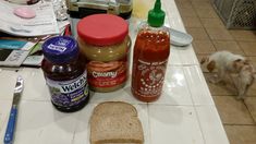 there are many condiments on the counter with bread and jam in front of them