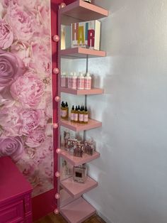 a pink shelf with lots of bottles on it in front of a floral wallpaper