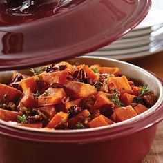 a red casserole dish filled with sweet potatoes and cranberries