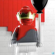 a lego man with a crown on his head holding a giant black balloon in front of a red wall