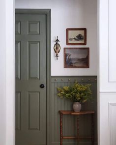 a green door in a white room with pictures on the wall and a small table next to it