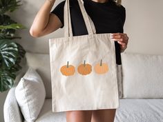 a woman holding a tote bag with three pumpkins on it