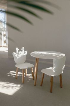 two white chairs and a table in an empty room with sunlight coming through the window