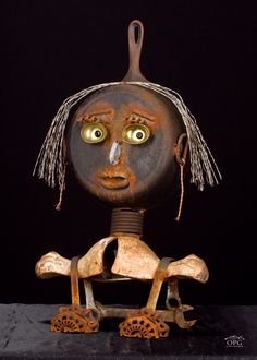 an old, rusty metal sculpture with eyes and hair on it's head is sitting in front of a black background