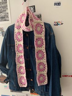 a denim jacket hanging on a wall with a crocheted scarf draped over it