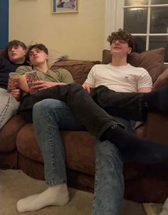 three young men sitting on a couch in a living room, one with his eyes closed