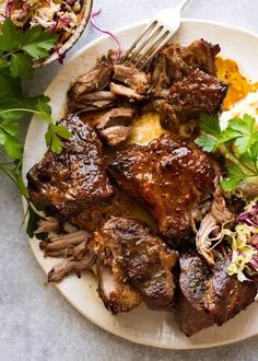 a white plate topped with meat and veggies next to a bowl of coleslaw