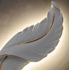 a wall light with a white feather design on it's side and gold trim around the edge