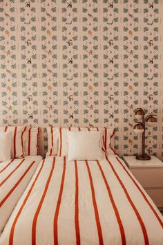 two twin beds in a bedroom with wallpaper and red and white bed linens