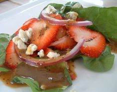 a white plate topped with spinach, strawberries and feta cheese covered in sauce