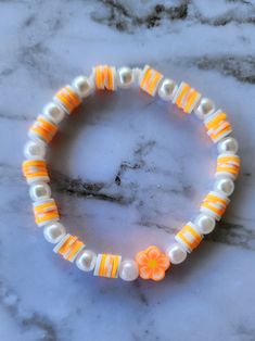 an orange and white beaded bracelet with flowers on it sitting on a marble surface