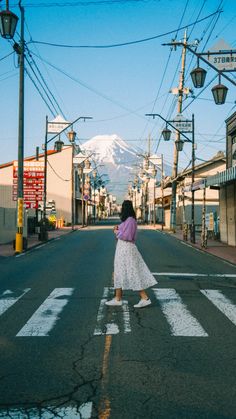 a woman crossing the street at an intersection in front of a snow covered mountain and telephone poles