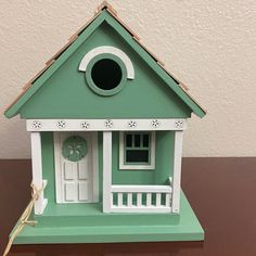 a green and white birdhouse with a clock on the front door, sitting on a table