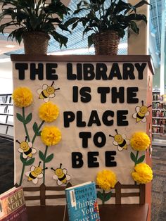 the library is the place to be sign with yellow flowers and bees on it next to bookshelves