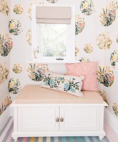 a white bench sitting under a window next to a wallpapered room with flowers on it