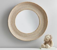 a teddy bear sitting next to a round mirror on a wall above a white shelf