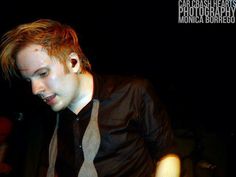 a young man with red hair wearing a black shirt and neck tie looking down at his cell phone