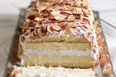 a slice of cake with white frosting and almonds on top is sitting on a glass platter