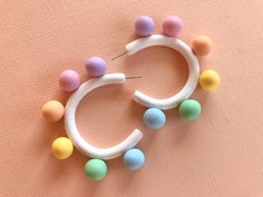 a pair of white hoop earrings with pastel colored balls hanging from it's sides