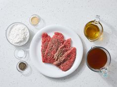 raw meat on a plate with spices and seasonings around it, next to a cup of tea