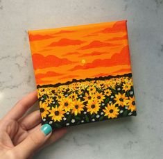 a hand is holding up a small painting with sunflowers in the foreground