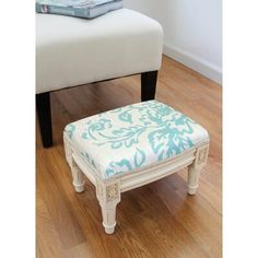 a white foot stool with a green and white pattern on the seat, next to a book