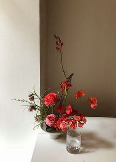 two vases filled with red flowers on top of a white table next to a wall