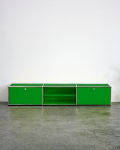 a green cabinet sitting on top of a cement floor next to a white wall in an empty room