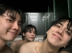 three young men are taking a bath in the shower stall, one is smiling at the camera