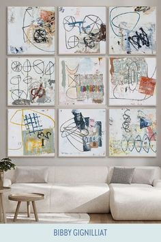 a living room with white furniture and paintings on the wall